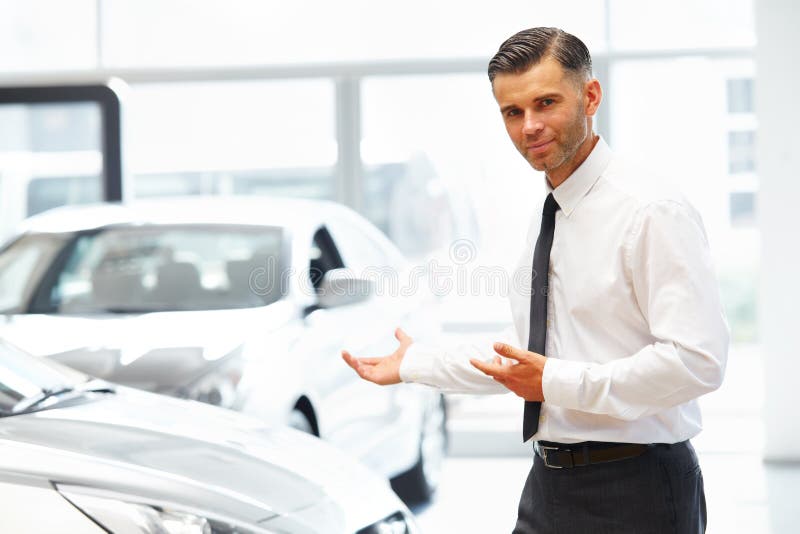 Salesman Standing at the Car Showroom and Showing New Cars stock photo Salesman Standing at the Car Showroom and Showing New Cars stock photo