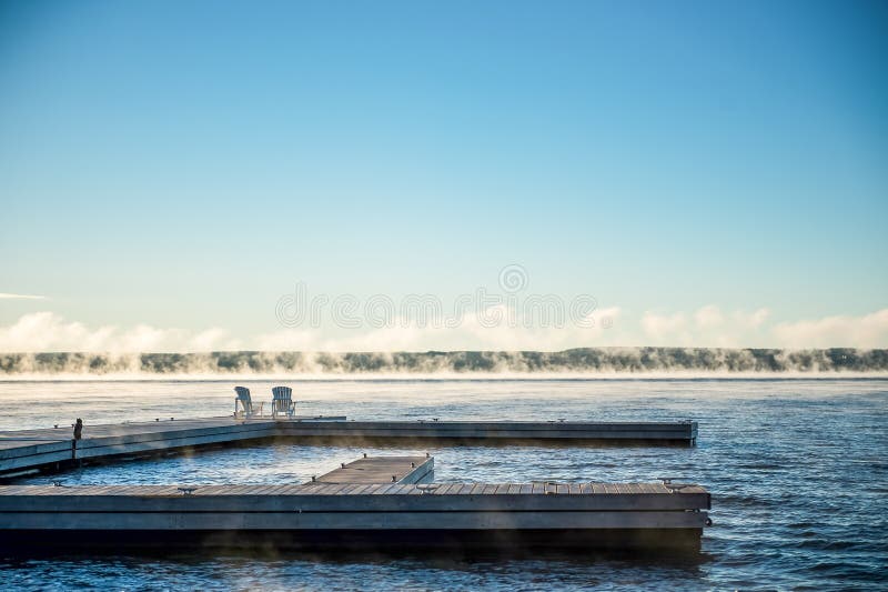 Salida del sol de la mañana en un muelle con las sillas y la niebla de Muskoka foto de archivo libre de regalías Salida del sol de la mañana en un muelle con las sillas y la niebla de Muskoka foto de archivo libre de regalías