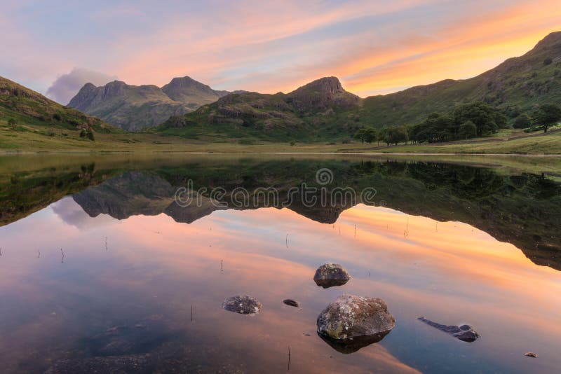 Vibrant sunrise with idyllic mirrored reflections in lake with rocks. Blea Tarn, Lake District, UK. Vibrant sunrise with idyllic mirrored reflections in lake with rocks. Blea Tarn, Lake District, UK.