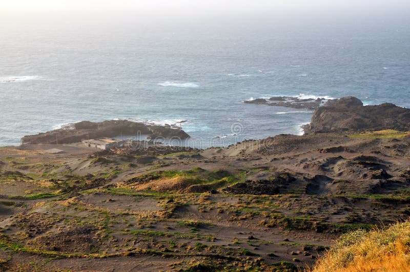 The bay of Salinas on the town of Sao Jorge with its surrounding black sand dunes sits below the cliff with its volcanic peninsula extending into the ocean. The bay of Salinas on the town of Sao Jorge with its surrounding black sand dunes sits below the cliff with its volcanic peninsula extending into the ocean