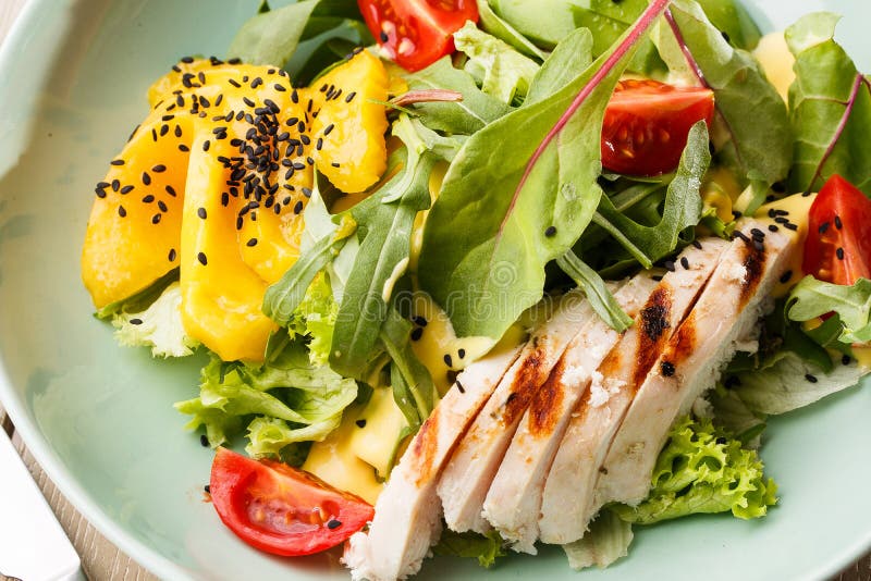 Sallad med grillad höna, mango, grönsallat, avokado, tomater, arugula, ostsause på en vit platta på trä arkivfoto Sallad med grillad höna, mango, grönsallat, avokado, tomater, arugula, ostsause på en vit platta på trä arkivfoto