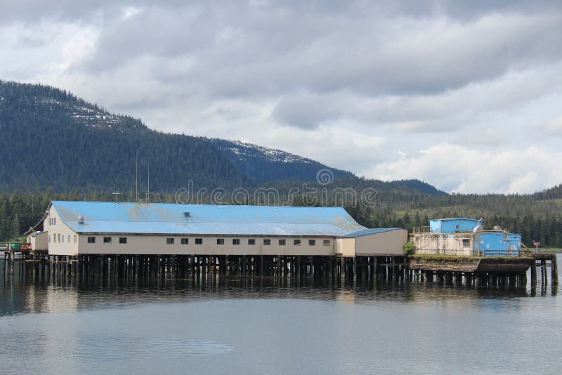 A salmon cannery on the end of a doc with a blue roof and mountain in background on Mitkof Island at the town of Petersburg, Alaska. A salmon cannery on the end of a doc with a blue roof and mountain in background on Mitkof Island at the town of Petersburg, Alaska.