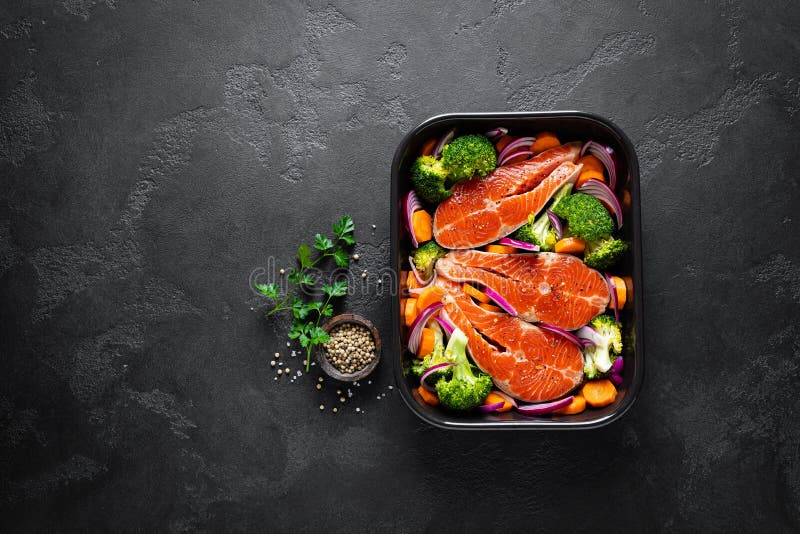 Salmon. Cooking fresh raw salmon fish steaks with vegetables, broccoli, carrot and onion on black background stock image Salmon. Cooking fresh raw salmon fish steaks with vegetables, broccoli, carrot and onion on black background stock image