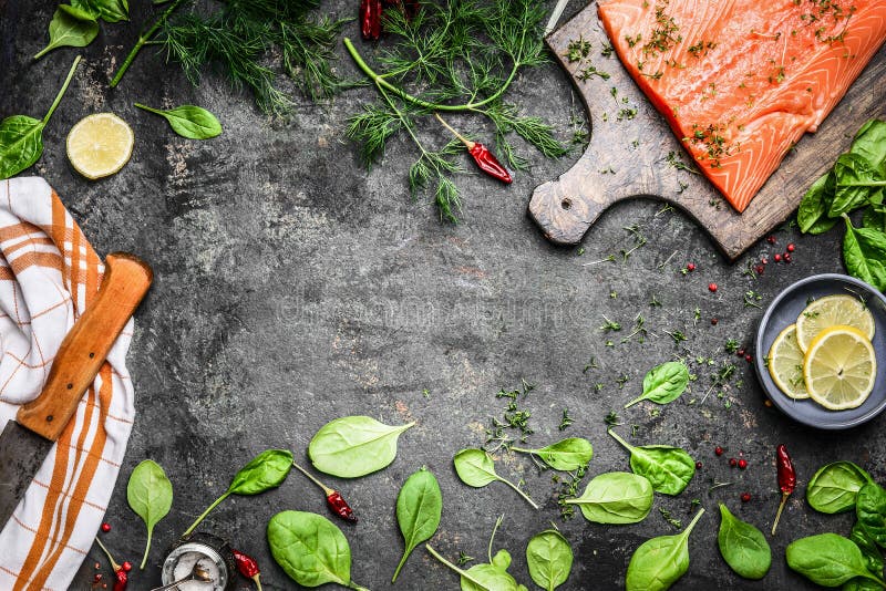 Salmon fish fillets on cutting board and fresh ingredients for cooking on rustic background, top view