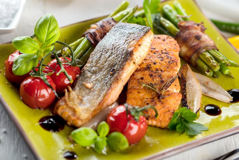 Salmones asados a la parrilla con las verduras servidas en la placa de piedra verde en la tabla de madera imágenes de archivo libres de regalías Salmones asados a la parrilla con las verduras servidas en la placa de piedra verde en la tabla de madera imágenes de archivo libres de regalías