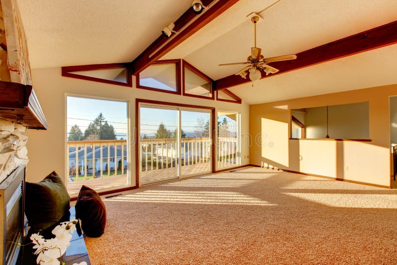 Living room with vaulted ceiling and beams, stoned background fireplace, beige carpet floor and walkout deck. Living room with vaulted ceiling and beams, stoned background fireplace, beige carpet floor and walkout deck