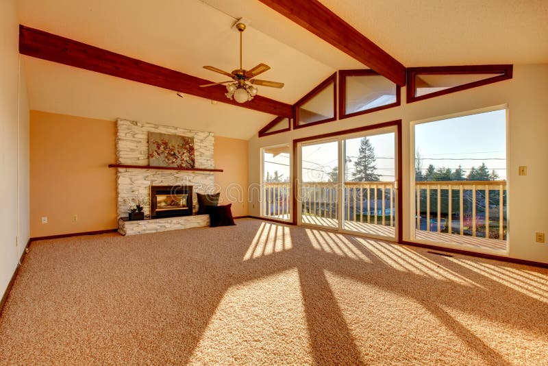 Living room with vaulted ceiling and beams, stoned background fireplace, beige carpet floor and walkout deck. Living room with vaulted ceiling and beams, stoned background fireplace, beige carpet floor and walkout deck