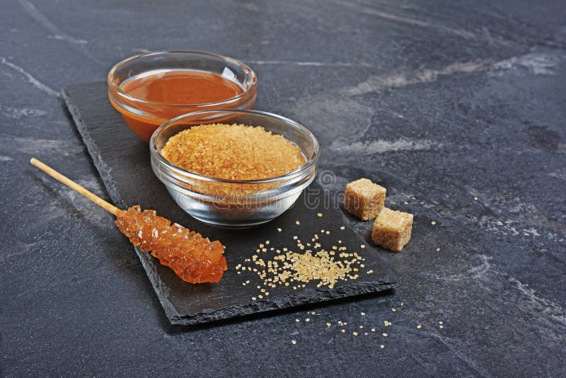 Salsa dolce casalinga del caramello in ciotola di vetro e zucchero di canna marrone con il bastone a cristallo dello zucchero immagine stock libera da diritti Salsa dolce casalinga del caramello in ciotola di vetro e zucchero di canna marrone con il bastone a cristallo dello zucchero immagine stock libera da diritti