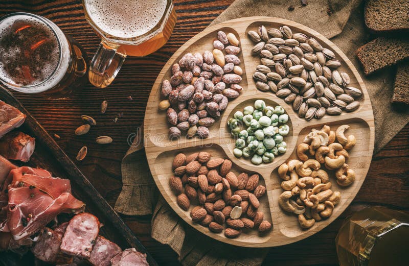 Salty snacks with nuts, fried corn, chips, smoked meat, sausage, prosciutto, cheese sticks and mugs with beer on wooden background