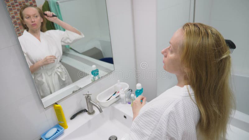 Salud del pelo, concepto de la pérdida de pelo Mujer que se peina el cabello seco dañado rubio en el cuarto de baño