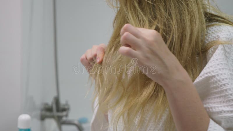 Salud del pelo, concepto de la pérdida de pelo Mujer que se peina el cabello seco dañado rubio en el cuarto de baño