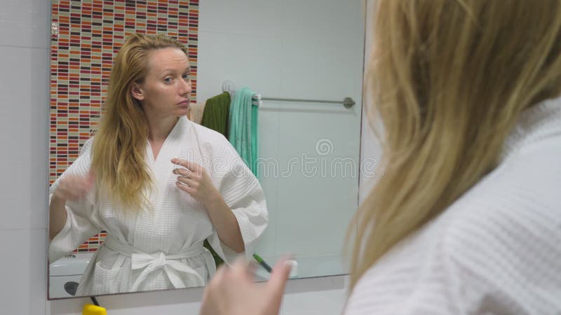 Salud del pelo, concepto de la pérdida de pelo Mujer que se peina el cabello seco dañado rubio en el cuarto de baño