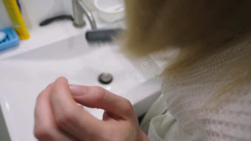 Salud del pelo, concepto de la pérdida de pelo Mujer que se peina el cabello seco dañado rubio en el cuarto de baño