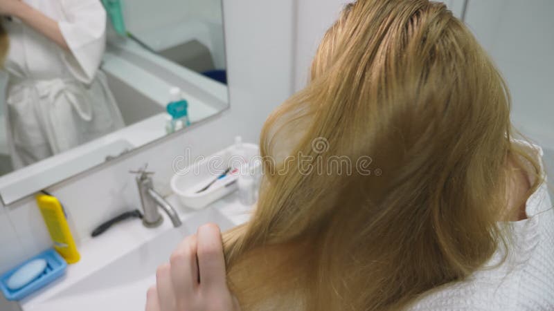 Salud del pelo, concepto de la pérdida de pelo Mujer que se peina el cabello seco dañado rubio en el cuarto de baño