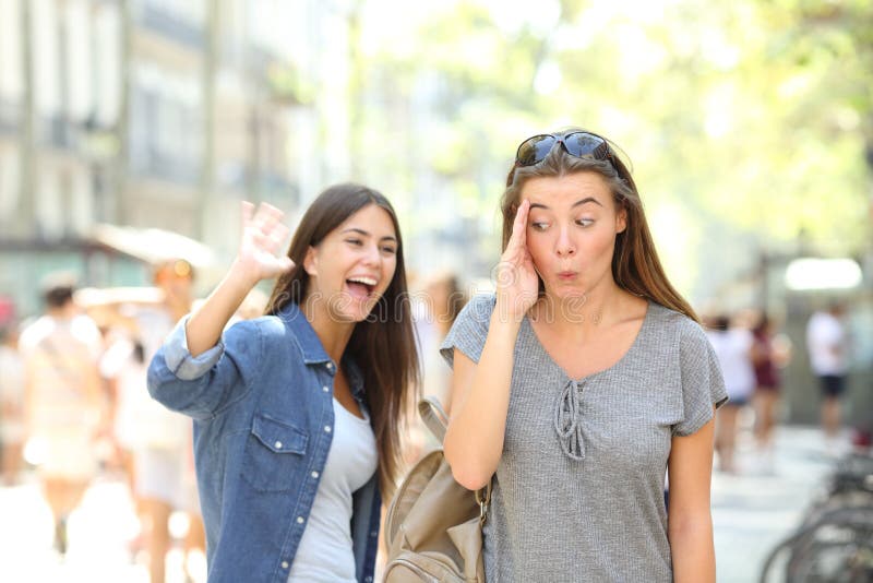 Happy teen greeting waving hand and friend ignoring her in the street. Happy teen greeting waving hand and friend ignoring her in the street