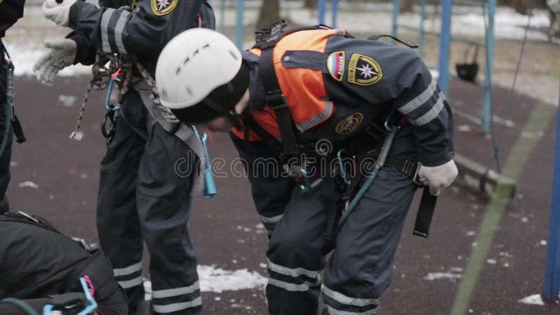 Salvadores jovenes en el casco, bolso del negro del lazo del equipo por una cuerda Entrenamiento de Emercom