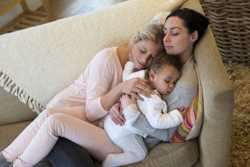 Same sex female couple sleeping with their baby son on their sofa at home. Same sex female couple sleeping with their baby son on their sofa at home