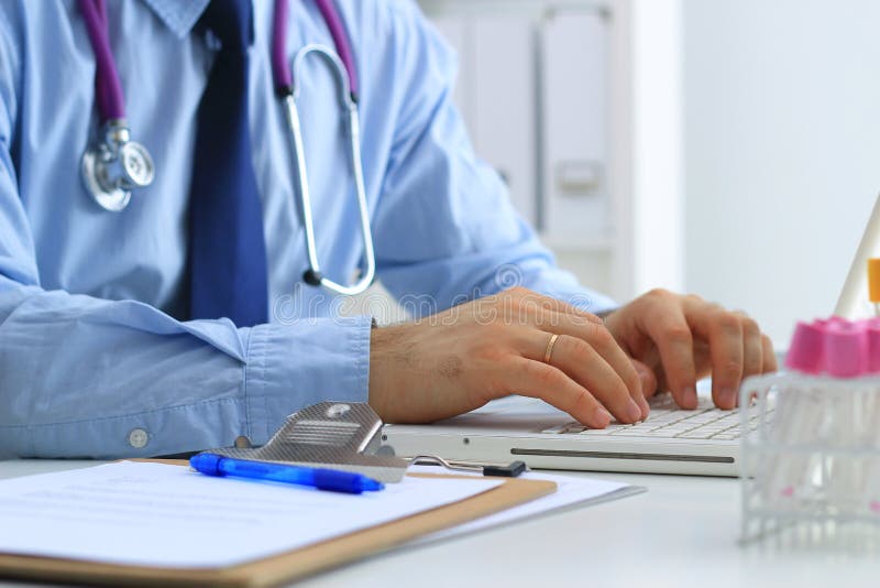 Samiec lekarka używa laptop, siedzi przy jego biurkiem obrazy stock Samiec lekarka używa laptop, siedzi przy jego biurkiem obrazy stock