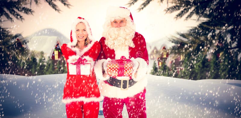 Sammansatt bild av santa och mrs claus som ler på den erbjudande gåvan för kamera arkivbild Sammansatt bild av santa och mrs claus som ler på den erbjudande gåvan för kamera arkivbild
