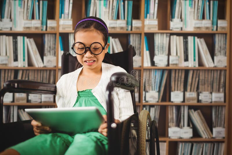 Young girl looking at digital tablet against various multi colored books on shelf. Young girl looking at digital tablet against various multi colored books on shelf