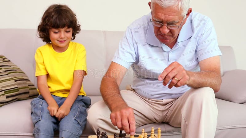 Sammanträde för hög man på soffan med hans sonson som spelar schack