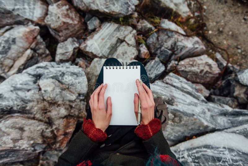 Sammanträde för konstnärflickamålning på vaggar på klippan, notepad Underbar nedgångsikt arkivbild Sammanträde för konstnärflickamålning på vaggar på klippan, notepad Underbar nedgångsikt arkivbild