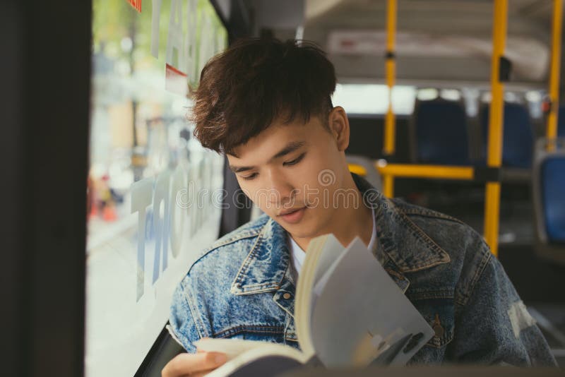 Sammanträde för ung man i stadsbuss och läsning en bok arkivfoton Sammanträde för ung man i stadsbuss och läsning en bok arkivfoton
