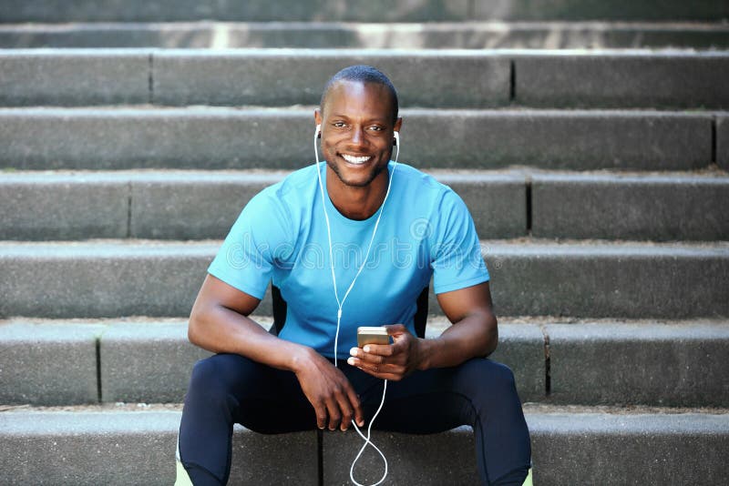 Smiling black guy sitting outside on stars with mobile phone and earphones. Smiling black guy sitting outside on stars with mobile phone and earphones