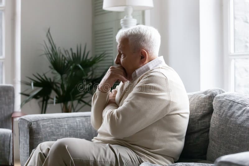 Grey haired old man sit on couch in living room alone, lost in sad pessimistic thoughts related to senile disease, mental disorder memory loss or dementia. Life troubles and lonely 80s person concept. Grey haired old man sit on couch in living room alone, lost in sad pessimistic thoughts related to senile disease, mental disorder memory loss or dementia. Life troubles and lonely 80s person concept