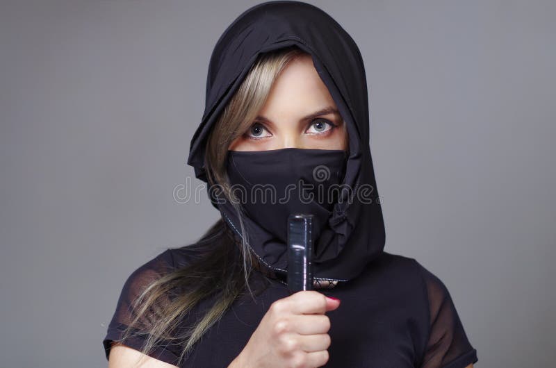 Samurai woman dressed in black with matching veil covering face, holding hand on sword facing camera, ninja concept royalty free stock photography Samurai woman dressed in black with matching veil covering face, holding hand on sword facing camera, ninja concept royalty free stock photography