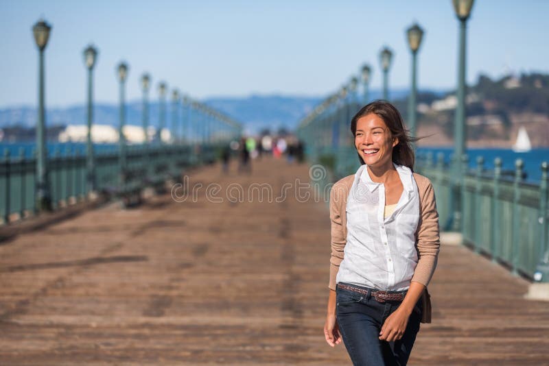 San Francisco travel lifestyle woman walking happy on pier. Asian girl smiling relaxing in harbor city in USA. San Francisco travel lifestyle woman walking happy on pier. Asian girl smiling relaxing in harbor city in USA