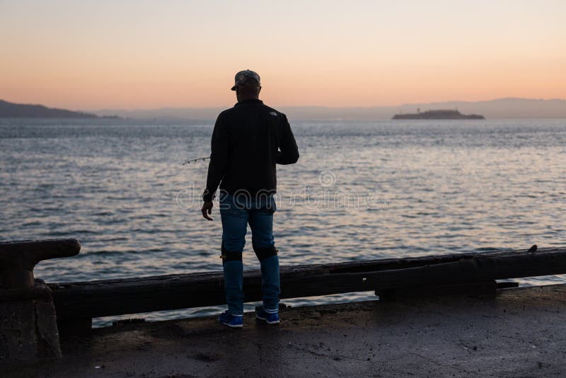 SAN FRANCISCO, USA - OCTOBER 12, 2018: Man fishing at sunrise with Alcatraz Island in the background stock photo SAN FRANCISCO, USA - OCTOBER 12, 2018: Man fishing at sunrise with Alcatraz Island in the background stock photo