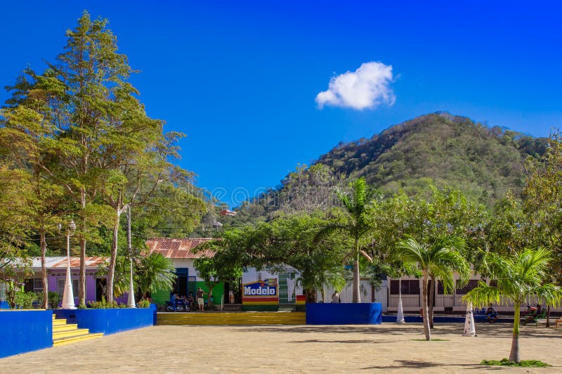 San Juan del Sur, Nicaragua - May 11, 2018: Outdoor view of park with some people sitting at outdoors of their houses in Juan del Sur, Nicaragua. It is main tourists destination and surfing capital. San Juan del Sur, Nicaragua - May 11, 2018: Outdoor view of park with some people sitting at outdoors of their houses in Juan del Sur, Nicaragua. It is main tourists destination and surfing capital.