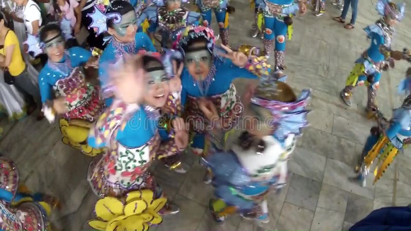 Boys and girls in ornate coconut costume wave on camera as they practice dancing