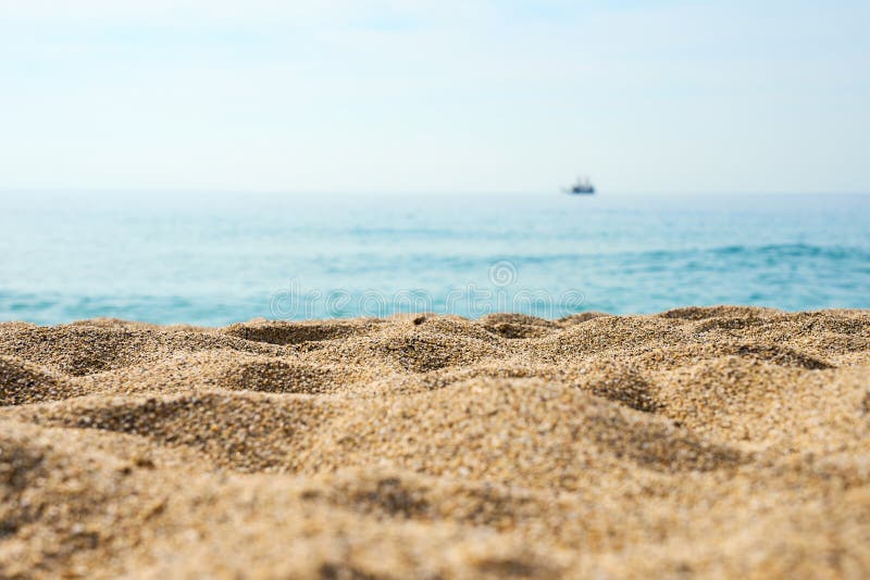 Sand on the beach close up with blurred sea, ship and waves on a background.