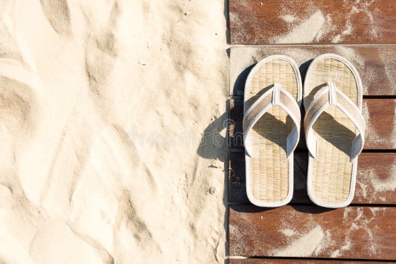 Sand and flip flops on boardwalk at sunny beach.