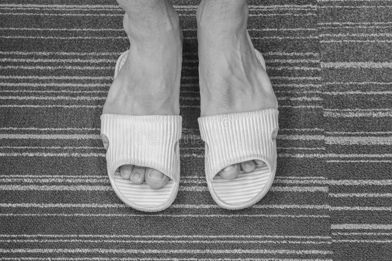 Sandale trop serrée noire et blanche de vêtements pour hommes sur ses pieds dans la maison photographie stock libre de droits Sandale trop serrée noire et blanche de vêtements pour hommes sur ses pieds dans la maison photographie stock libre de droits