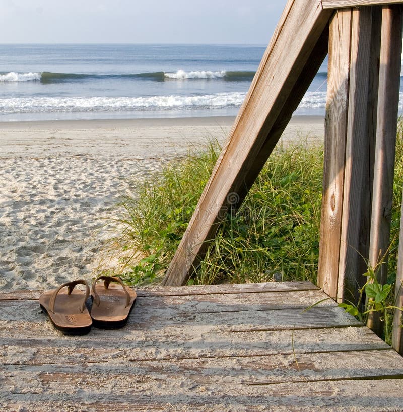 Sandály na pláži s pískem, vlny a nebe v pozadí na Sunset Beach, North Carolina.