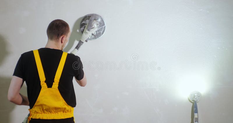 Sanding Walls for Painting. Worker in yellow work suit sanding the wall before painting using special sanding tool wall stock video