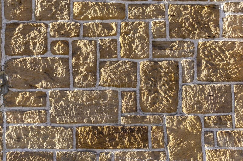 Sandstenvägg, bricked med den olika storleksanpassade vässade lantliga stenen och vita skarvar royaltyfri foto