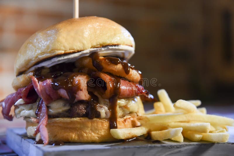 Hamburger sandwich with open brioche bread cream cheese fries bacon sauces on the table on blurred background. Hamburger sandwich with open brioche bread cream cheese fries bacon sauces on the table on blurred background.