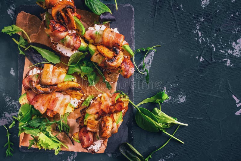 Sanduíche do abacate com o pão caseiro do ciabatta, cozinhado com o abacate cortado fresco e bacon e cogumelos friáveis fritados fotografia de stock Sanduíche do abacate com o pão caseiro do ciabatta, cozinhado com o abacate cortado fresco e bacon e cogumelos friáveis fritados fotografia de stock