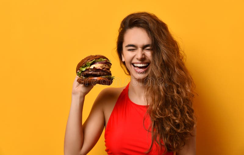 Sanduíche grande do hamburguer do assado da posse da mulher com riso gritando feliz da boca com fome no fundo amarelo imagens de stock Sanduíche grande do hamburguer do assado da posse da mulher com riso gritando feliz da boca com fome no fundo amarelo imagens de stock