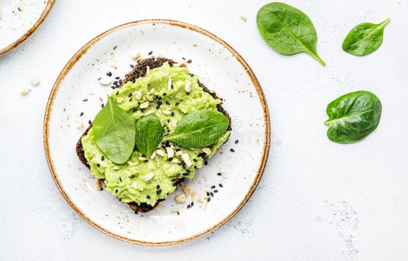 Sandviș cu avocado sau pâine prăjită pe pâine de secară cu nuci de cajou zdrobite cu spanac și semințe de susan pe fond alb de mas stock images