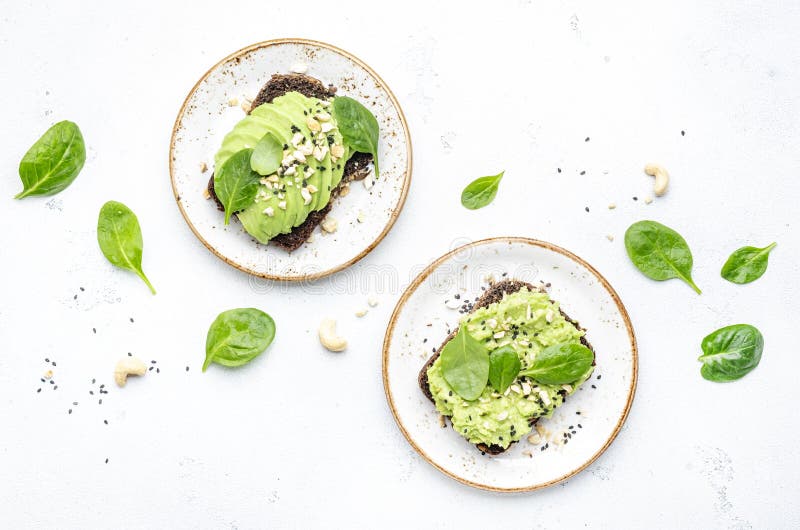 Sandviș cu avocado sau pâine prăjită pe pâine de secară cu nuci de cajou zdrobite cu spanac și semințe de susan pe fond alb de mas royalty free stock photography