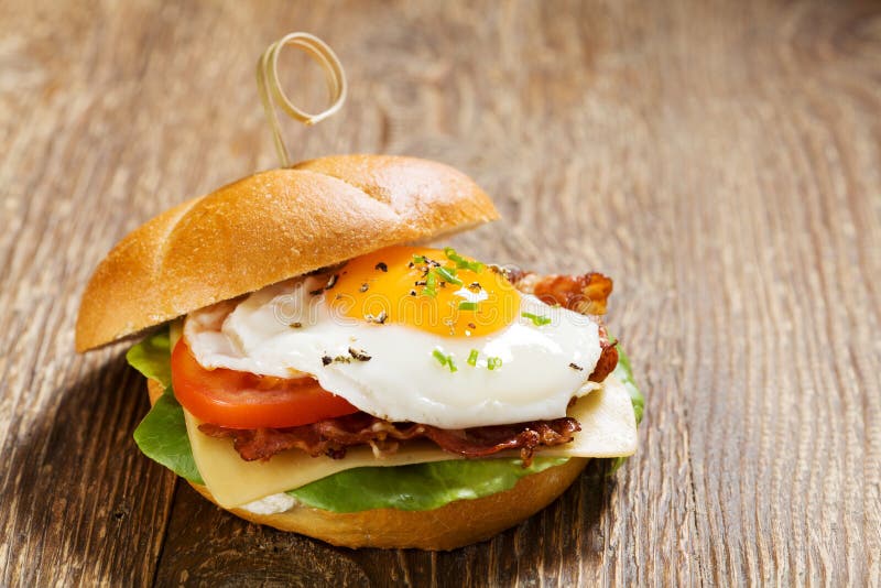 Sandwich with a Fried Egg, Bacon, Cheese and Vegetables Stock Photo