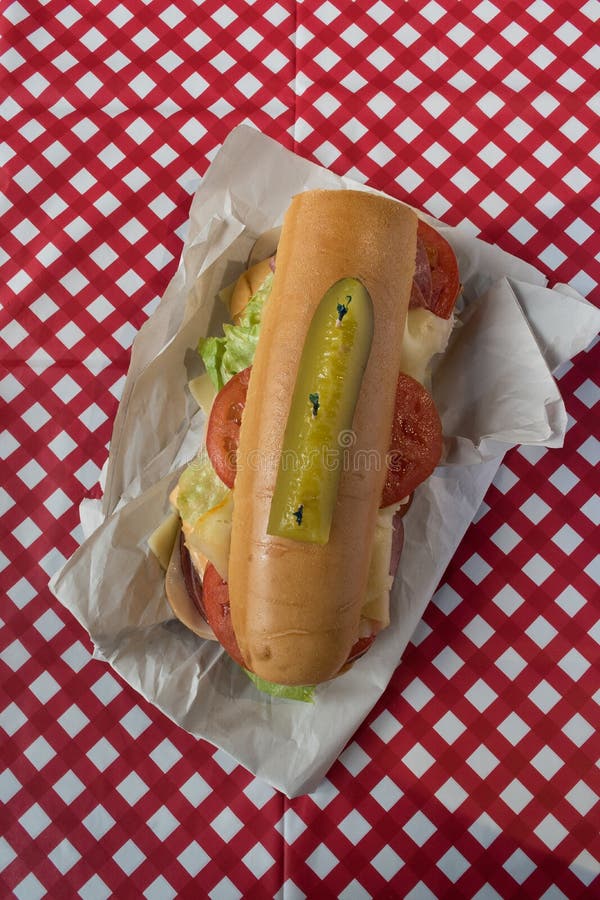 Sandwich with Lettuce, Tomato, Cheese, Pickle, and Sliced Meat on Patterned Tablecloth Stock