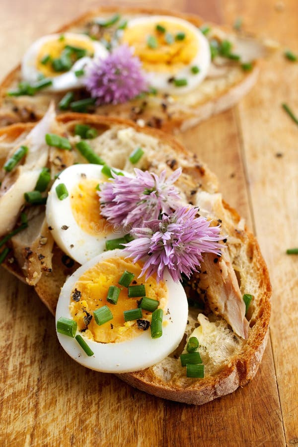 Sandwich met adition van makreelvissen, eieren en eetbare bloemen van bieslook op houten lijst stock afbeelding Sandwich met adition van makreelvissen, eieren en eetbare bloemen van bieslook op houten lijst stock afbeelding