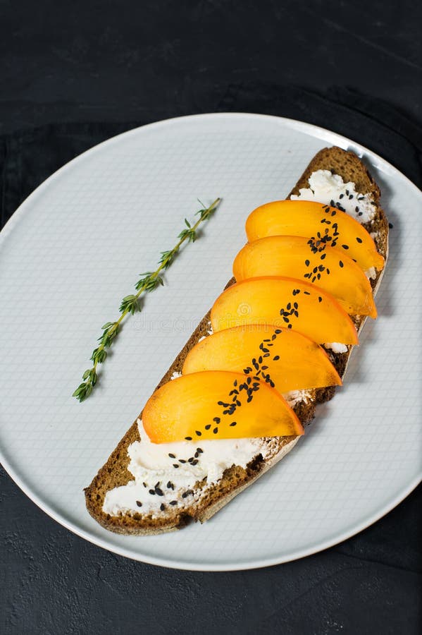 Sandwich ?quilibr? sain ? nourriture avec le kaki et fromage ? p?te molle sur le fond noir photographie stock libre de droits Sandwich ?quilibr? sain ? nourriture avec le kaki et fromage ? p?te molle sur le fond noir photographie stock libre de droits