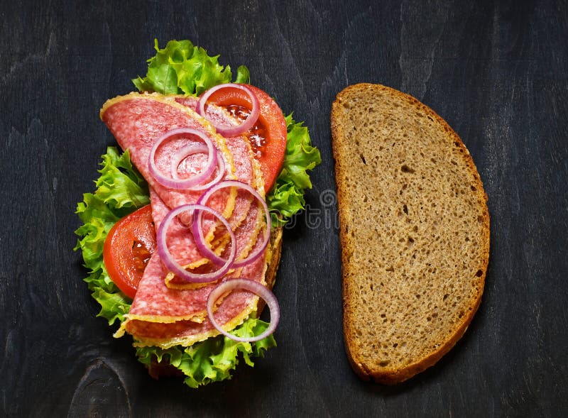 Sandwich with Tomato, Salami, Salad, Onion on Dark Background. Stock